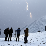 **A group of tourists stranded in a blizzard on Fansipan mountain while trying to observe a meteor shower. Emphasize the harsh weather conditions (heavy snow, strong winds, low visibility) and the tourists' panic.**